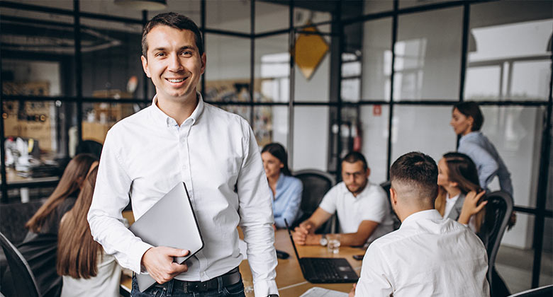 Man smiling in front of a meeting room full of employees